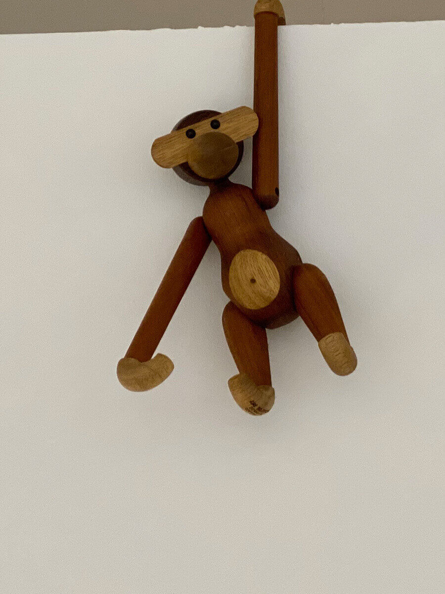 Ein Holzaffe hängt an einer weißen Wand